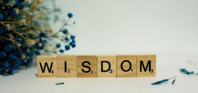 a wooden block spelling the word wisdom next to a bouquet of flowers by Alex Shute courtesy of Unsplash.