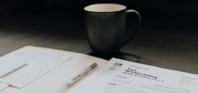 coffee mug near open folder with tax withholding paper by Kelly Sikkema courtesy of Unsplash.
